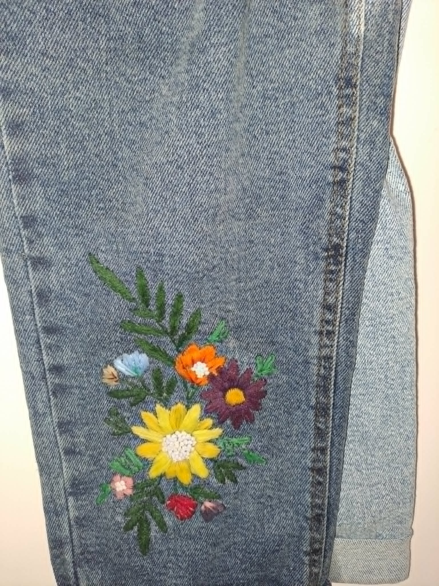 broderie à la main d'un bouquet de fleurs multicolores avec feuillage sur la jambe d'un jean