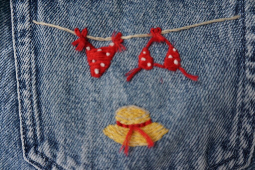 broderie à la main d'un bikini rouge à pois suspendu à un fil et d'un chapeau de paille sur la poche arrière d'un short en jean à plat