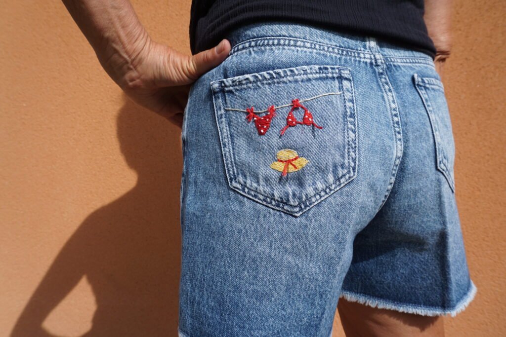 broderie à la main d'un bikini rouge à pois et d'un chapeau de paille sur la poche arrière d'un short en jean porté, vue rapprochée