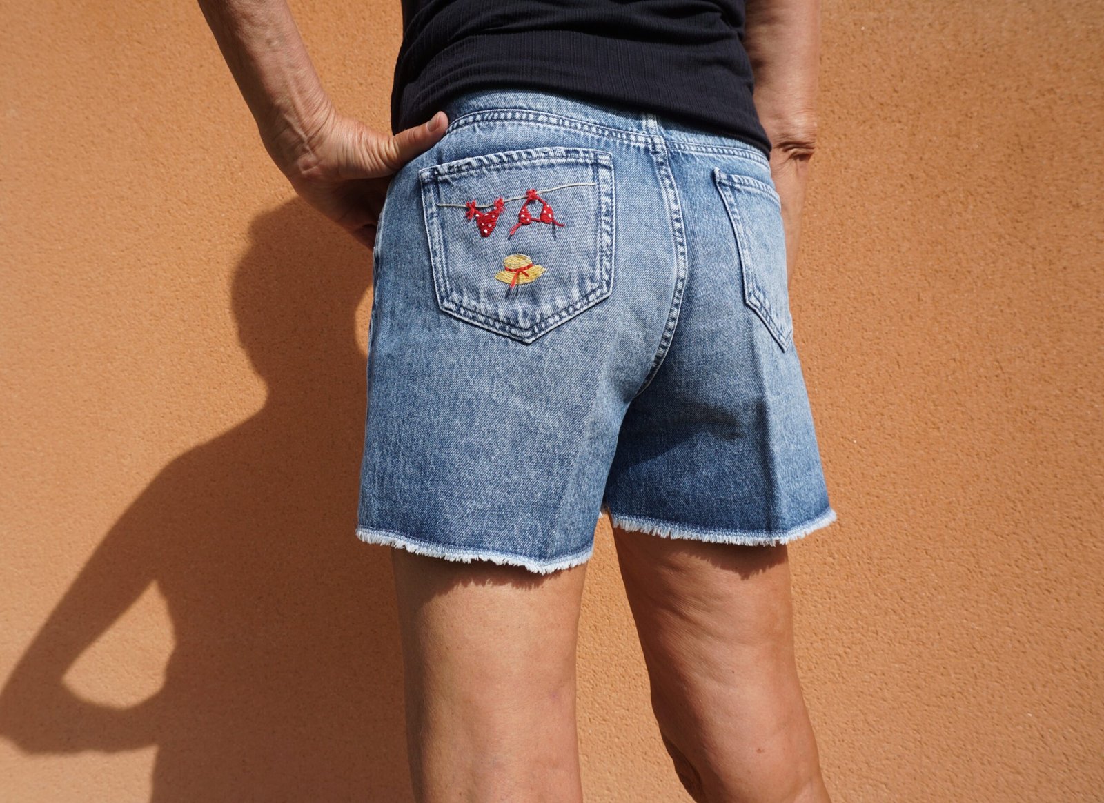 broderie à la main d'un bikini rouge à pois et d'un chapeau de paille sur la poche arrière d'un short en jean porté, vu de dos