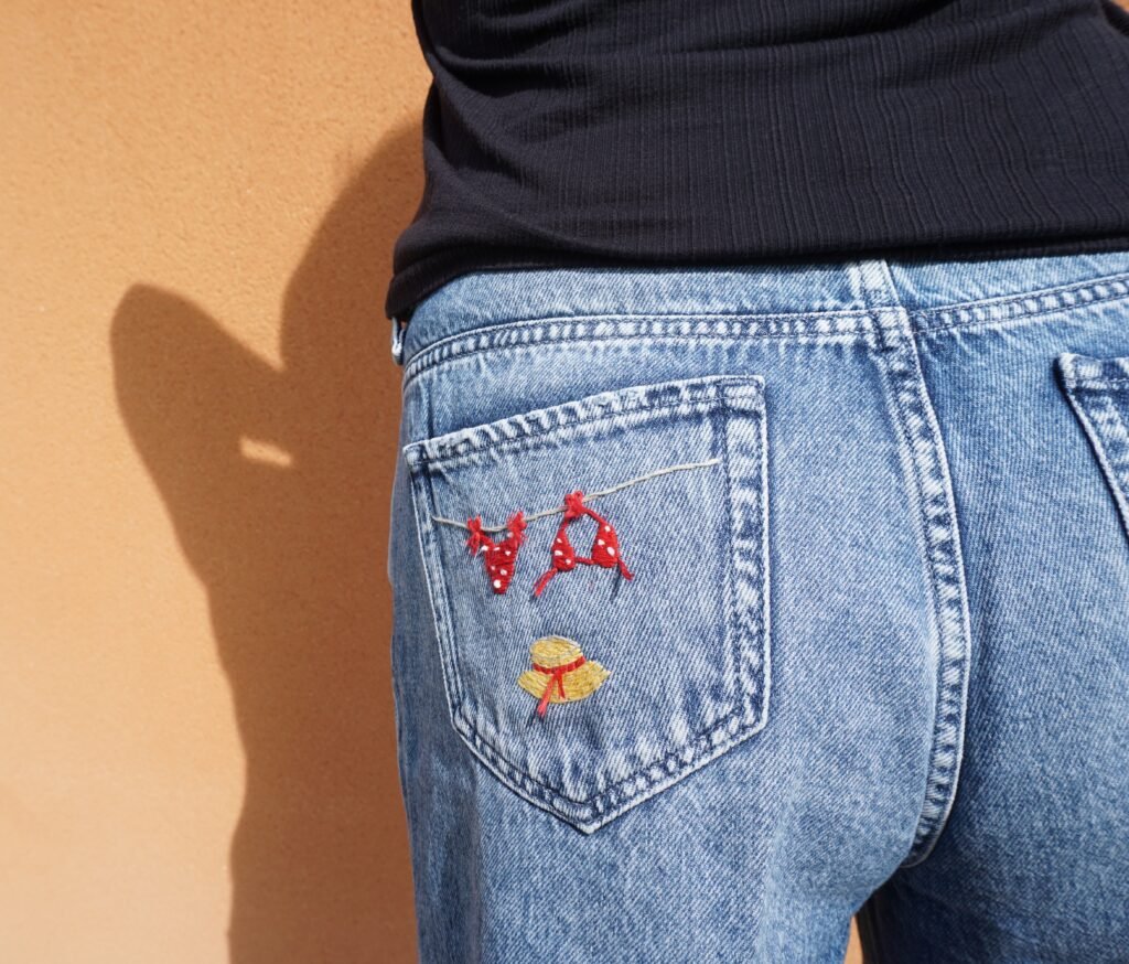 gros plan sur la poche arrière d'un short en jean porté, brodée à la main d'un bikini rouge à pois et d'un chapeau de paille