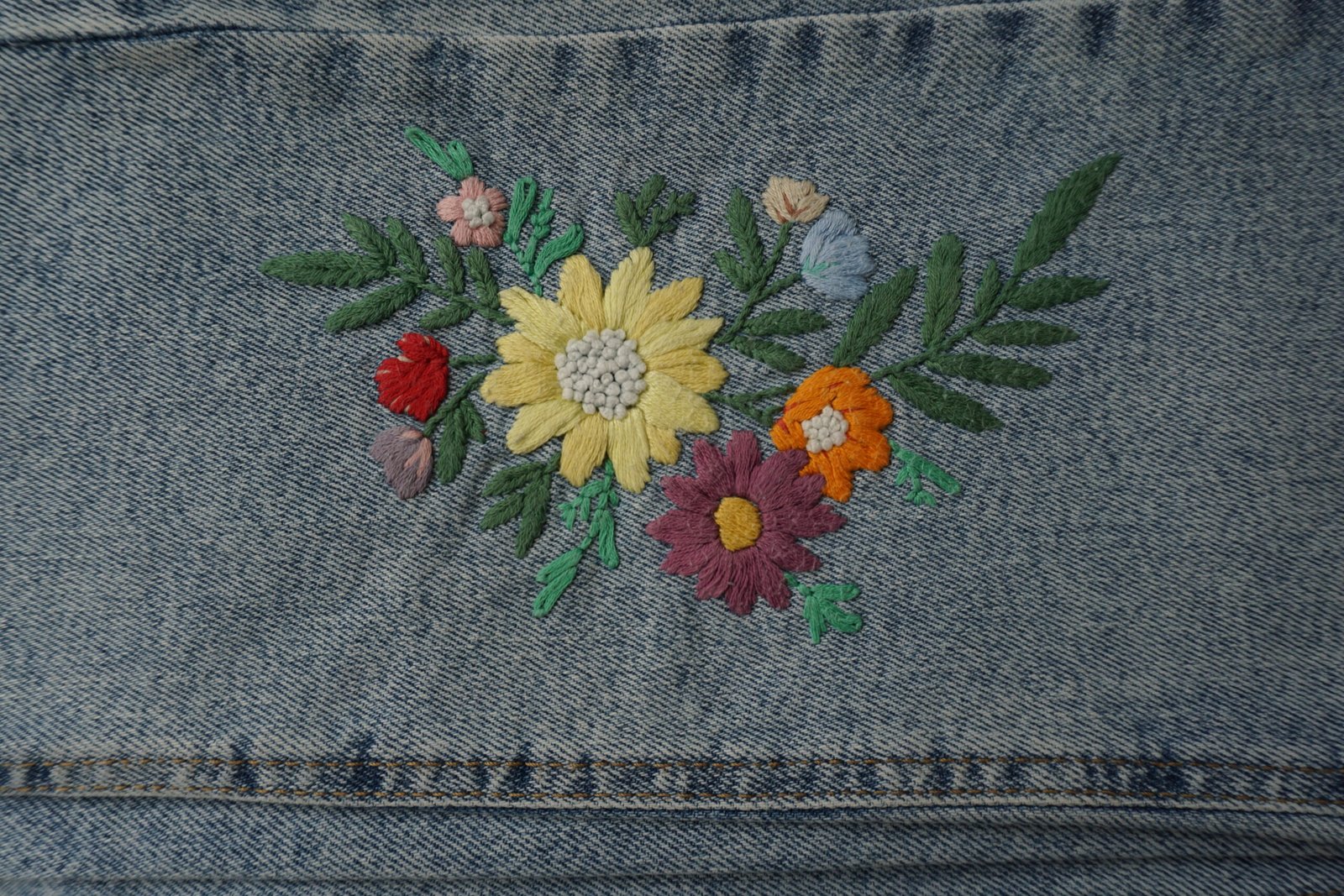 vue rapprochée d'un bouquet de fleurs multicolores brodé à la main sur le bas d'une jambe de jean à plat