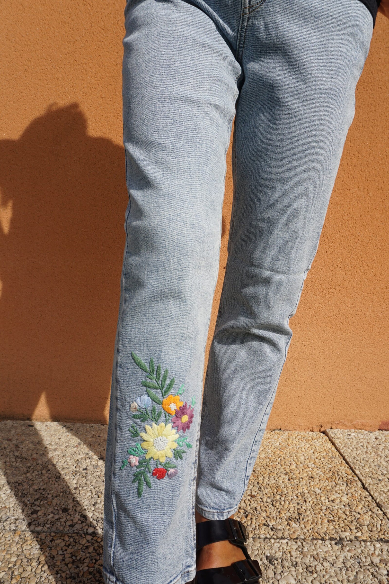 broderie à la main d'un bouquet de fleurs sur le bas de la jambe d'un jean porté, vue en pied