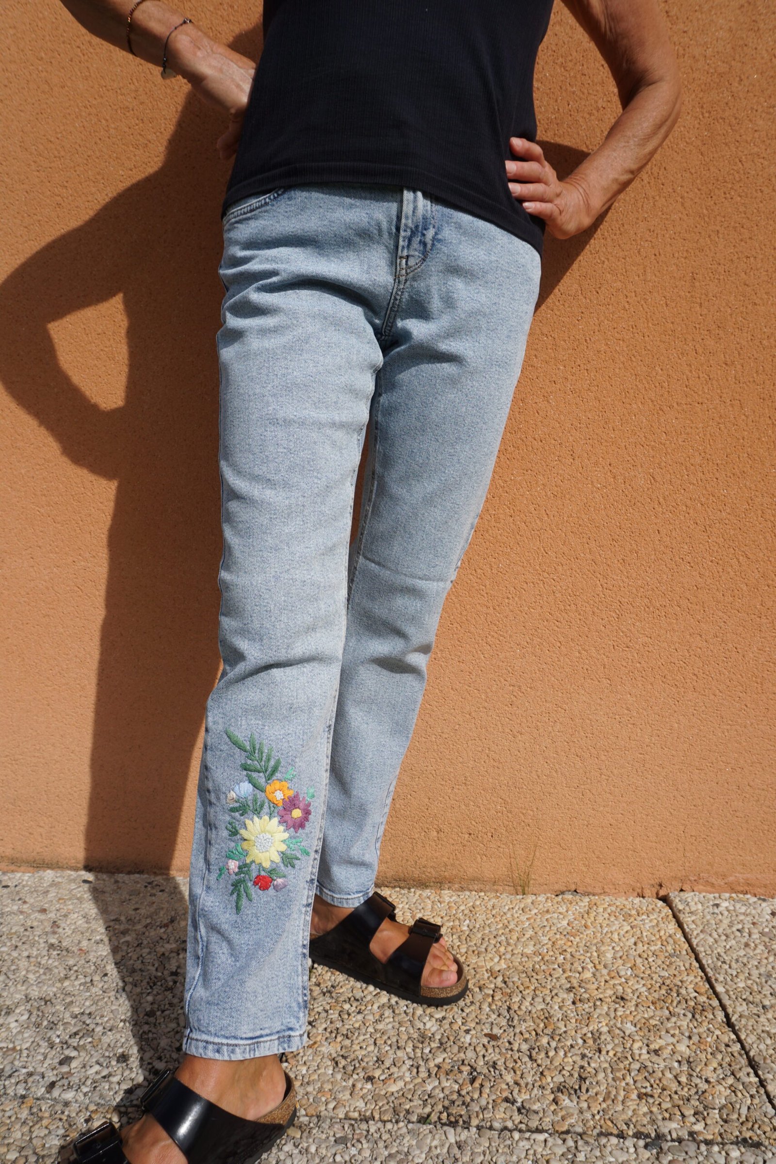 broderie à la main d'un bouquet de fleurs multicolores sur le bas de la jambe d'un jean porté, vu de face
