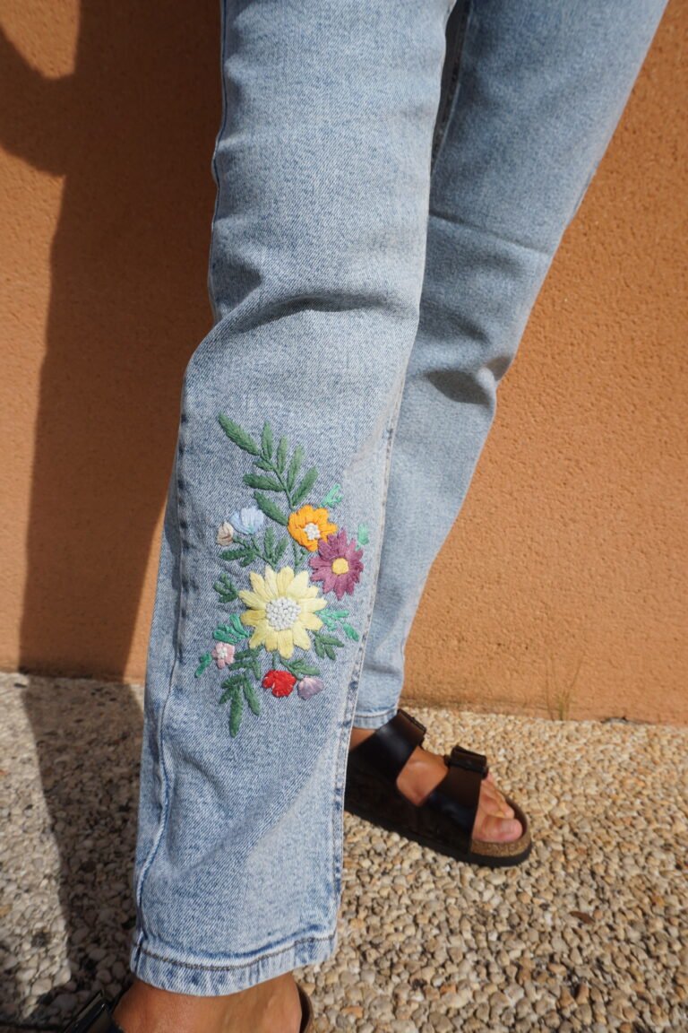 broderie à la main d'un bouquet de fleurs multicolores sur la jambe d'un jean porté, vue rapprochée