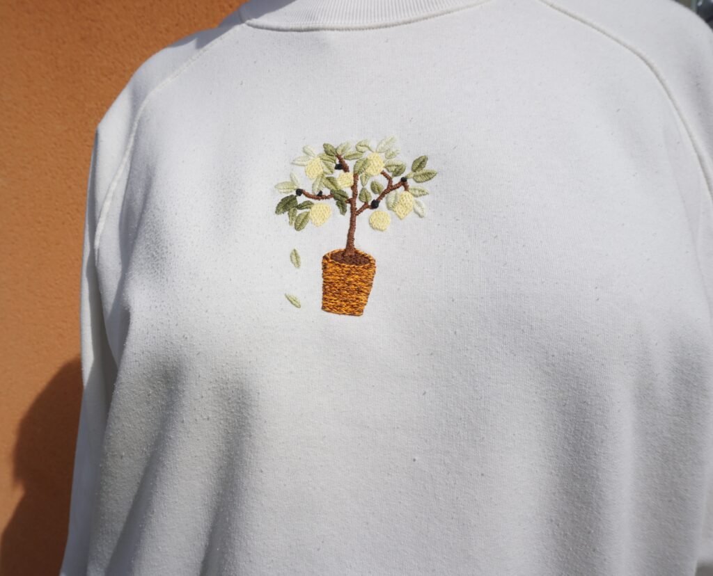 broderie à la main d'un citronnier en pot sur un sweat écru, vue rapprochée