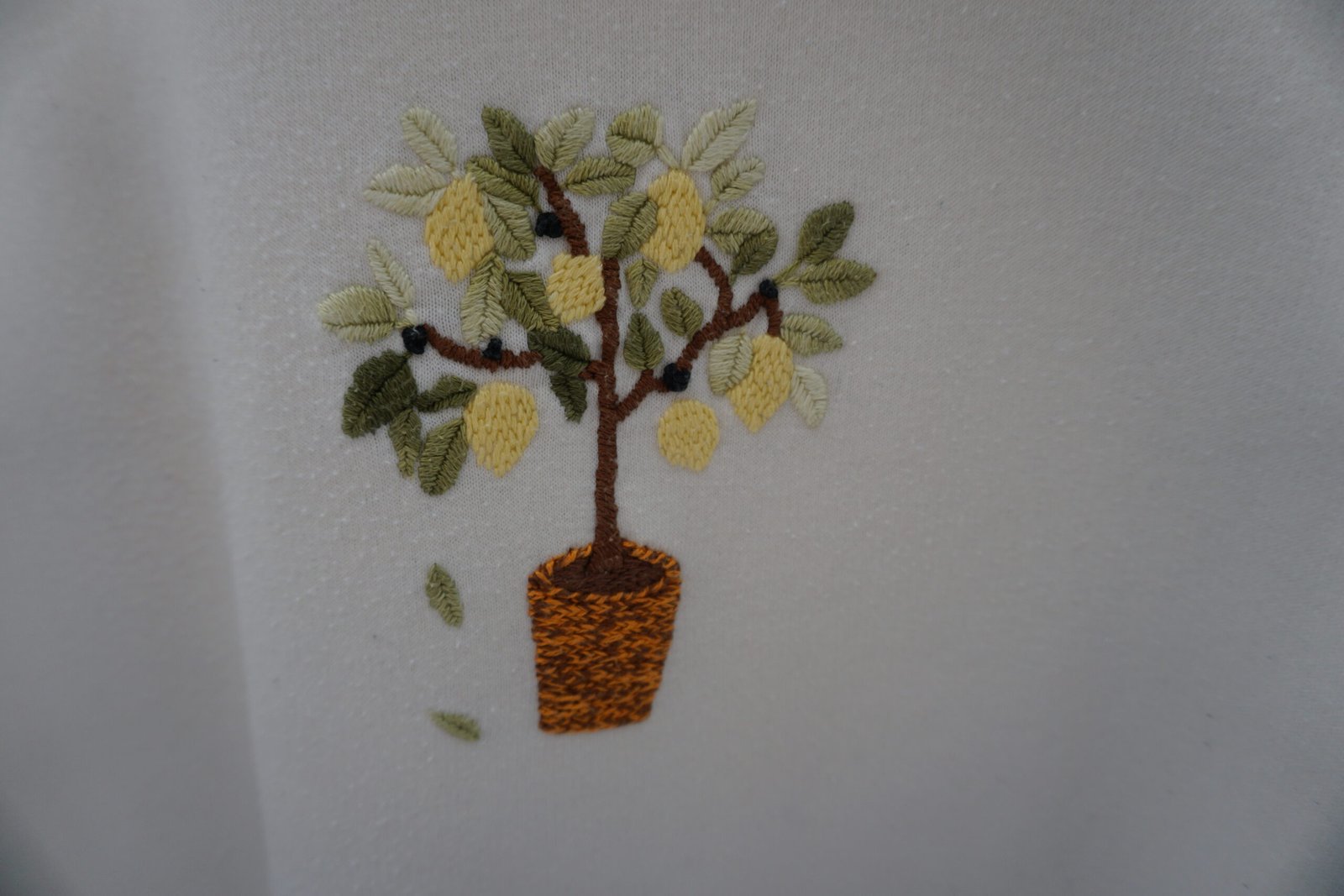 broderie à la main d'un citronnier en pot sur un sweat écru à plat