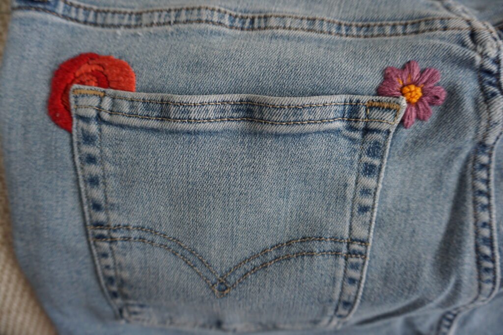 broderie à la main d'un coquelicot rouge et d'une fleur rose aux coins d'une poche arrière de jean clair à plat