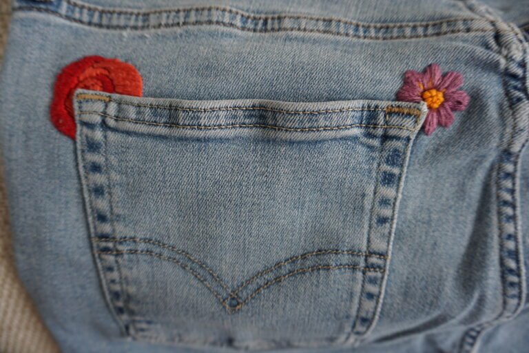 broderie à la main d'un coquelicot rouge et d'une fleur rose aux coins d'une poche arrière de jean clair à plat