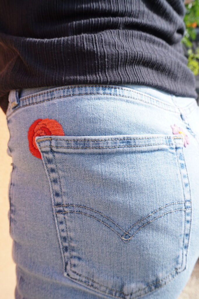 broderie à la main d'un coquelicot rouge au coin de la poche arrière d'un jean clair porté, vu de profil