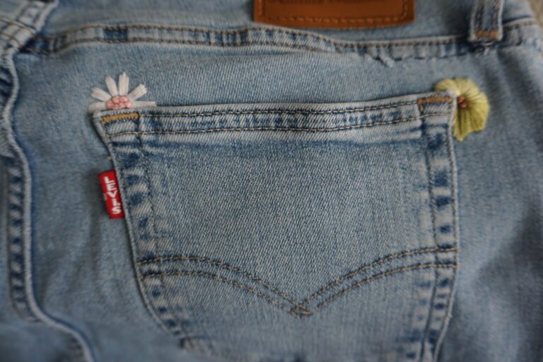 broderie à la main d'une marguerite et d'une fleur jaune aux coins d'une poche arrière de jean clair à plat