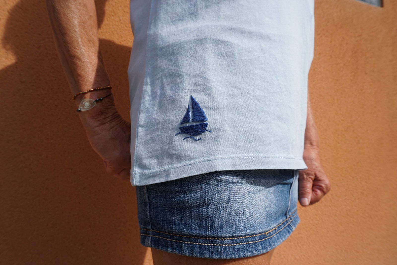 broderie à la main d'un petit voilier bleu sur le bas d'un tee-shirt bleu clair porté, vue rapprochée