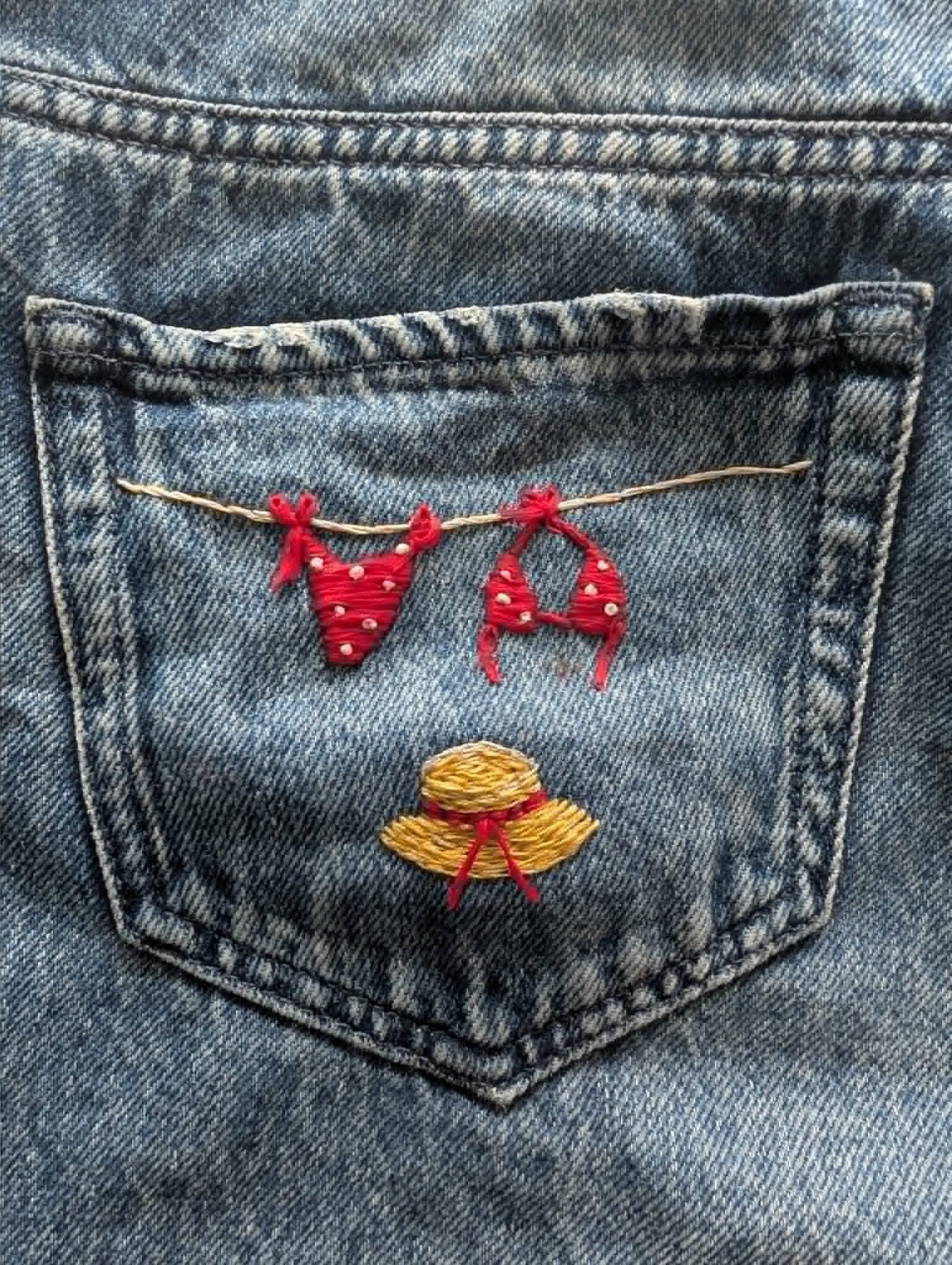 broderie à la main d'un bikini rouge à pois suspendu à un fil à linge et d'un chapeau de paille sur la poche d'un short en jean