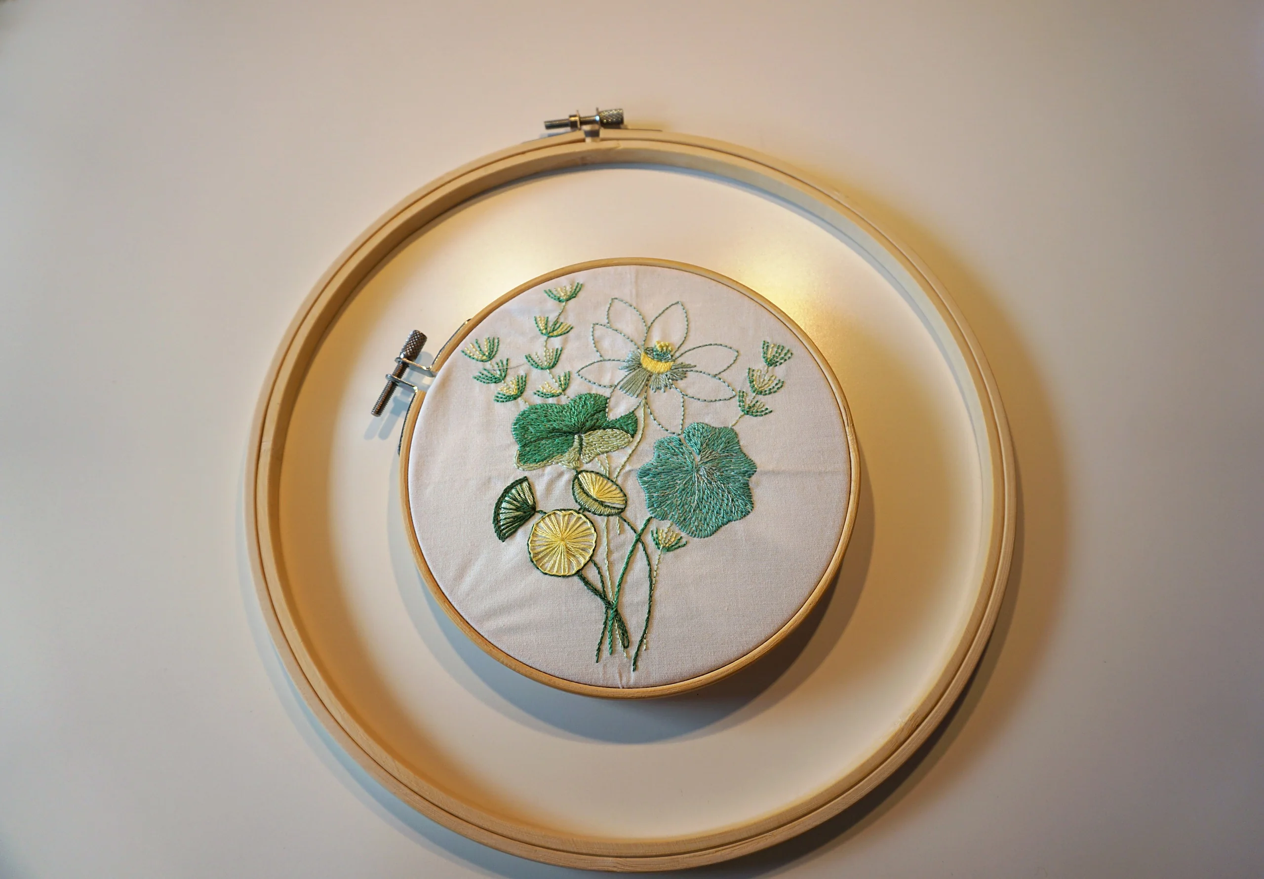 tambour à broder avec un nénuphar et ses feuilles en cours de broderie à la main, posé sur un second tambour